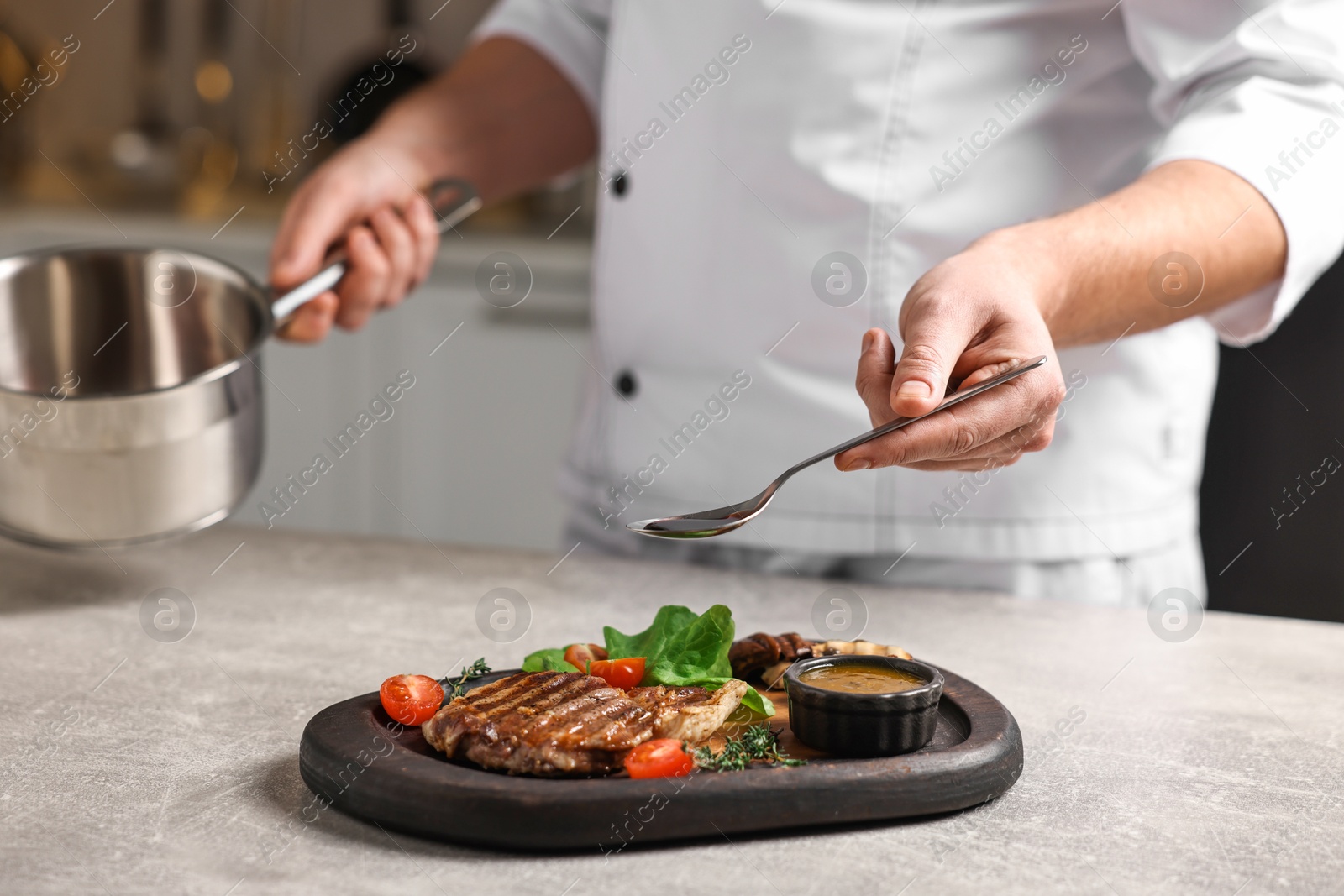 Photo of Professional chef adding sauce to delicious dish at table indoors, closeup