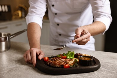 Photo of Professional chef adding sauce to delicious dish at table indoors, closeup