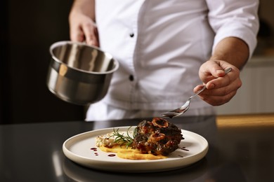 Photo of Professional chef adding sauce to delicious dish at table indoors, closeup