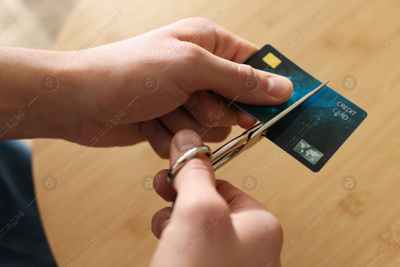 Photo of Man cutting credit card at wooden table indoors, closeup