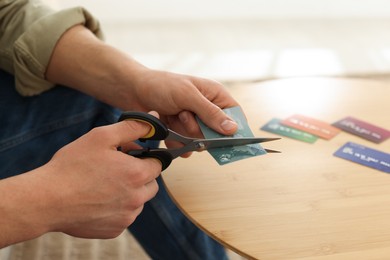 Photo of Man cutting credit card at wooden table indoors, closeup