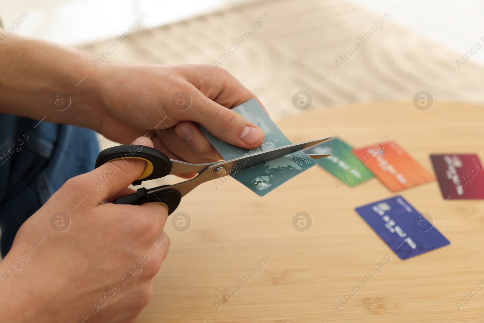 Photo of Man cutting credit card at wooden table indoors, closeup