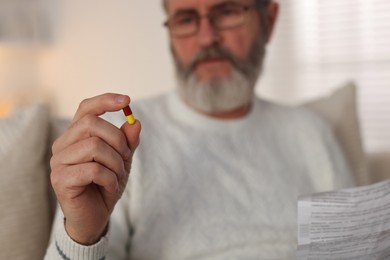 Photo of Senior man with pill and instruction indoors, selective focus