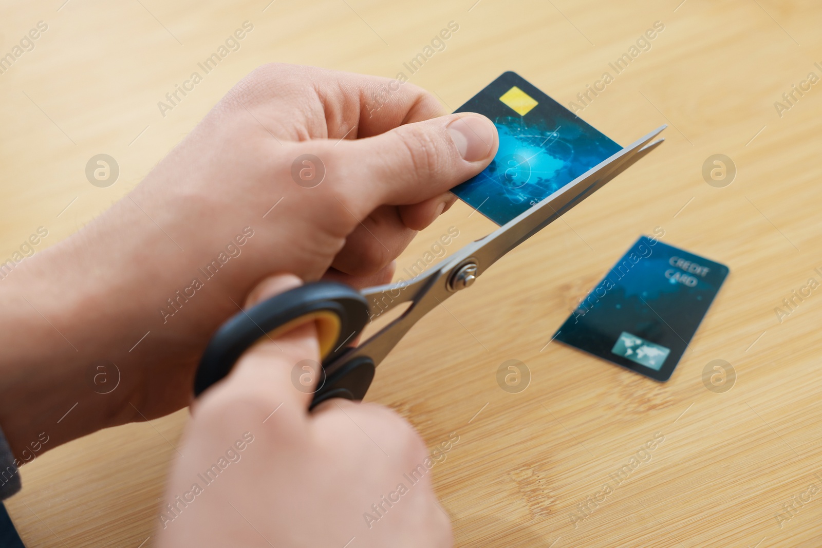 Photo of Man cutting credit card at wooden table indoors, closeup