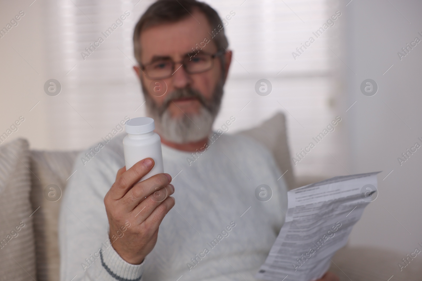 Photo of Senior man with bottle of pills and instruction at home, selective focus