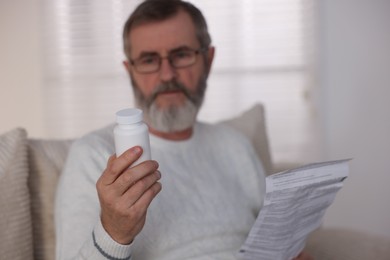 Photo of Senior man with bottle of pills and instruction at home, selective focus