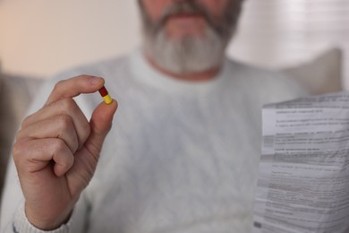 Photo of Senior man with pill and instruction at home, closeup