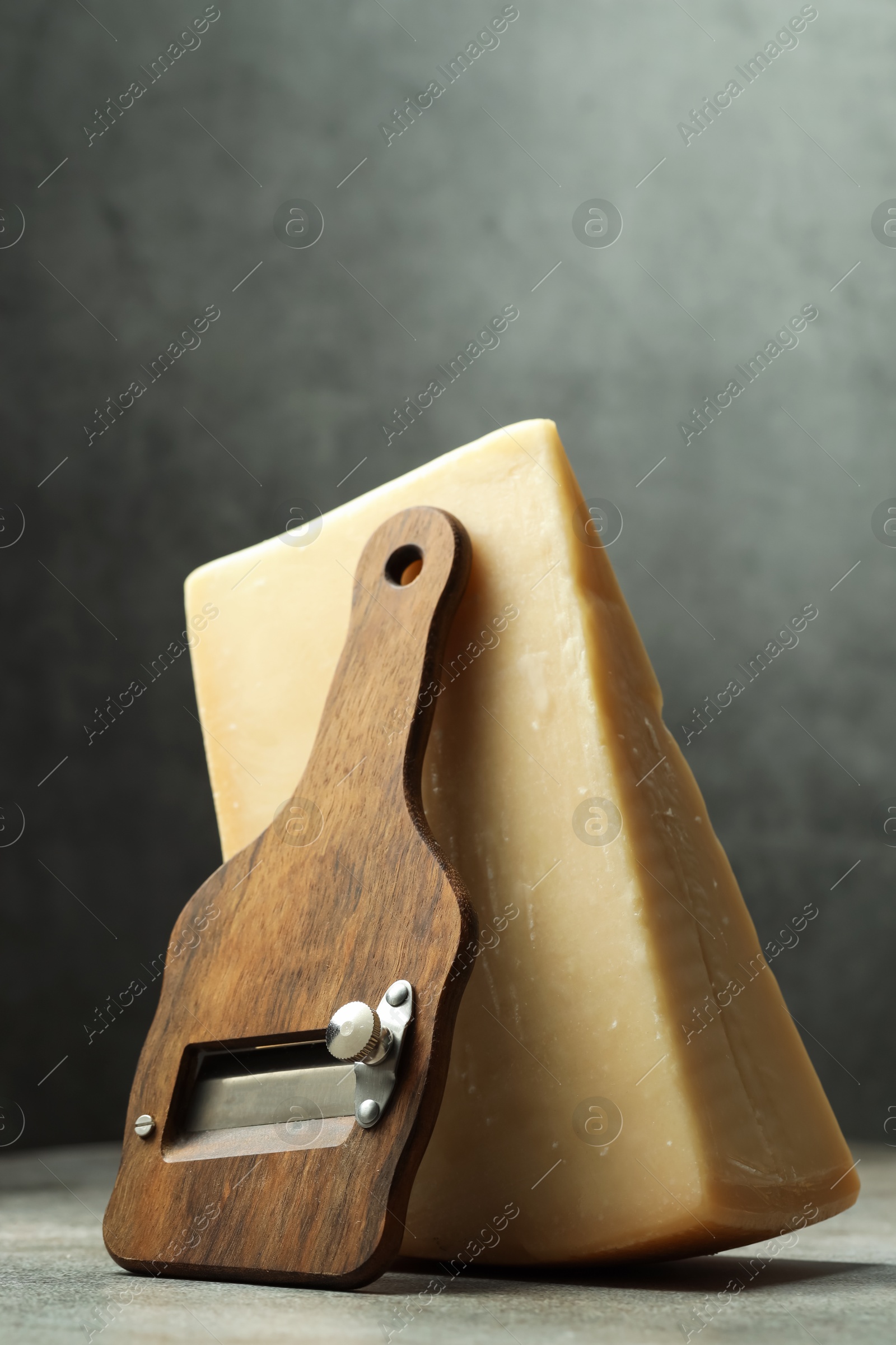 Photo of Piece of tasty cheese and slicer on grey table, closeup