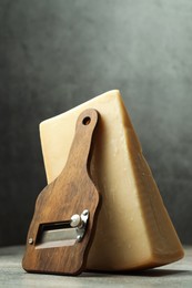 Photo of Piece of tasty cheese and slicer on grey table, closeup