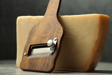 Photo of Piece of tasty cheese and slicer on grey table, closeup