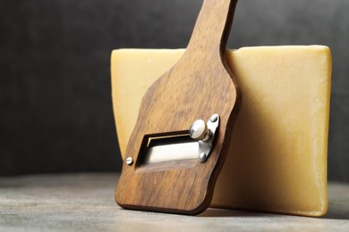 Photo of Piece of tasty cheese and slicer on grey table, closeup. Space for text