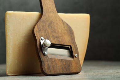 Photo of Piece of tasty cheese and slicer on grey table, closeup