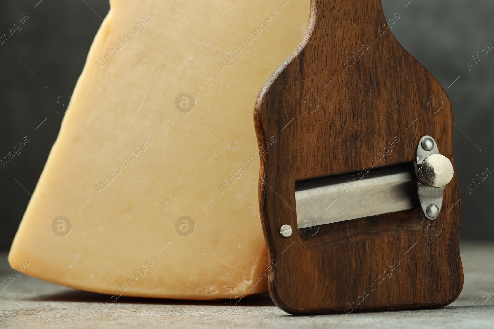 Photo of Piece of tasty cheese and slicer on grey table, closeup