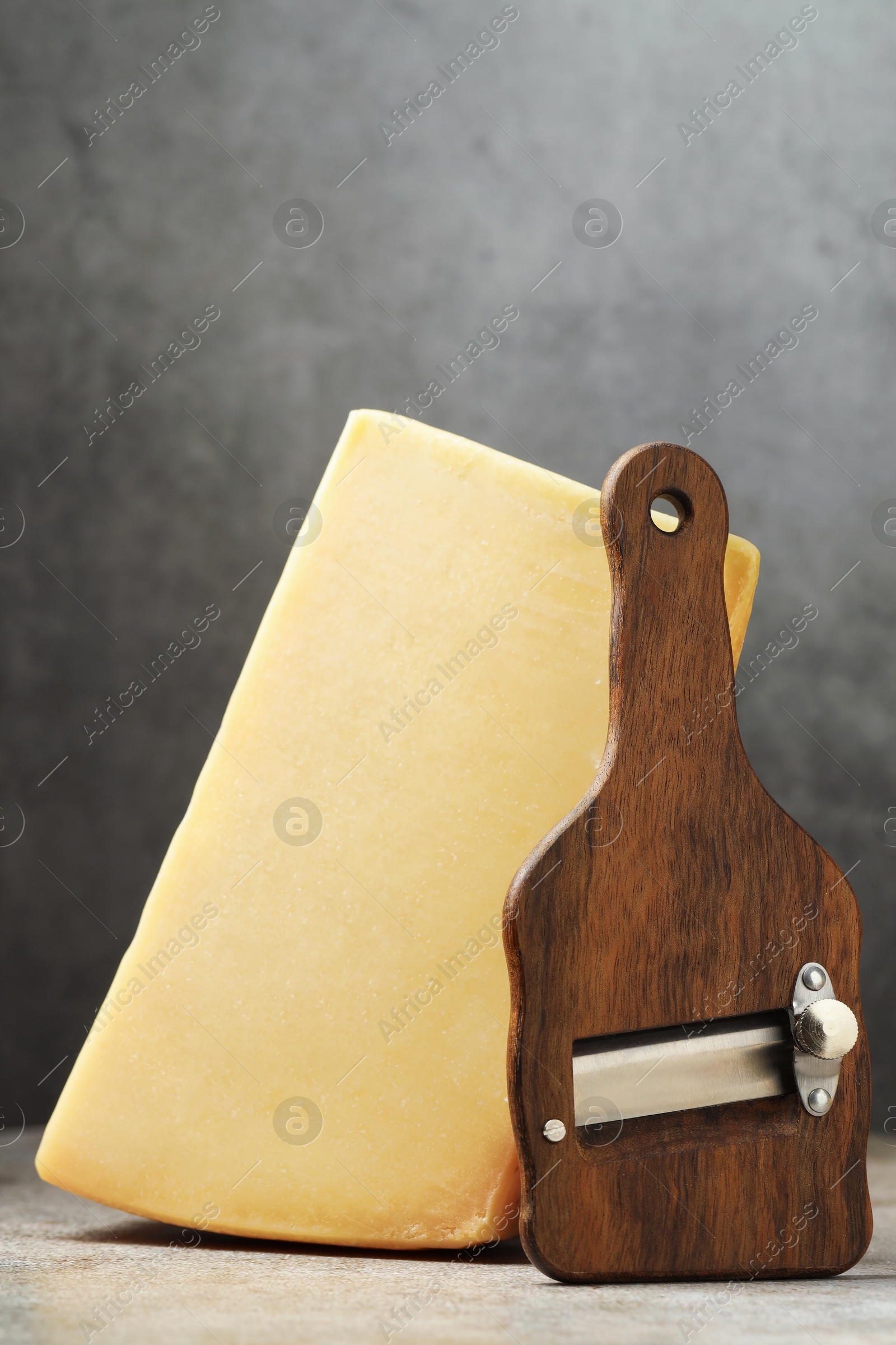 Photo of Piece of tasty cheese and slicer on grey table