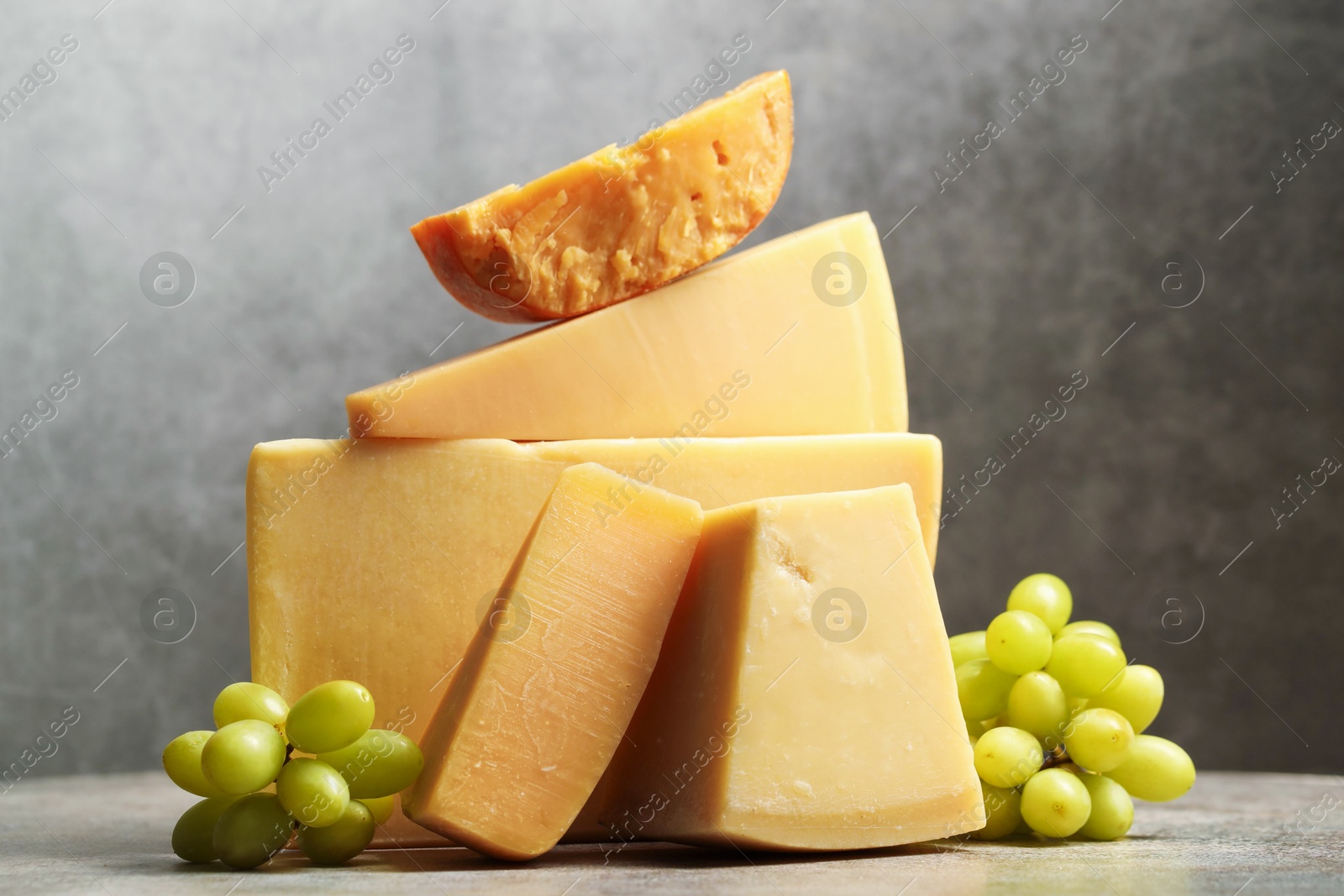 Photo of Different types of cheese and grapes on grey table