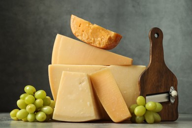 Photo of Different types of cheese, slicer and grapes on grey table