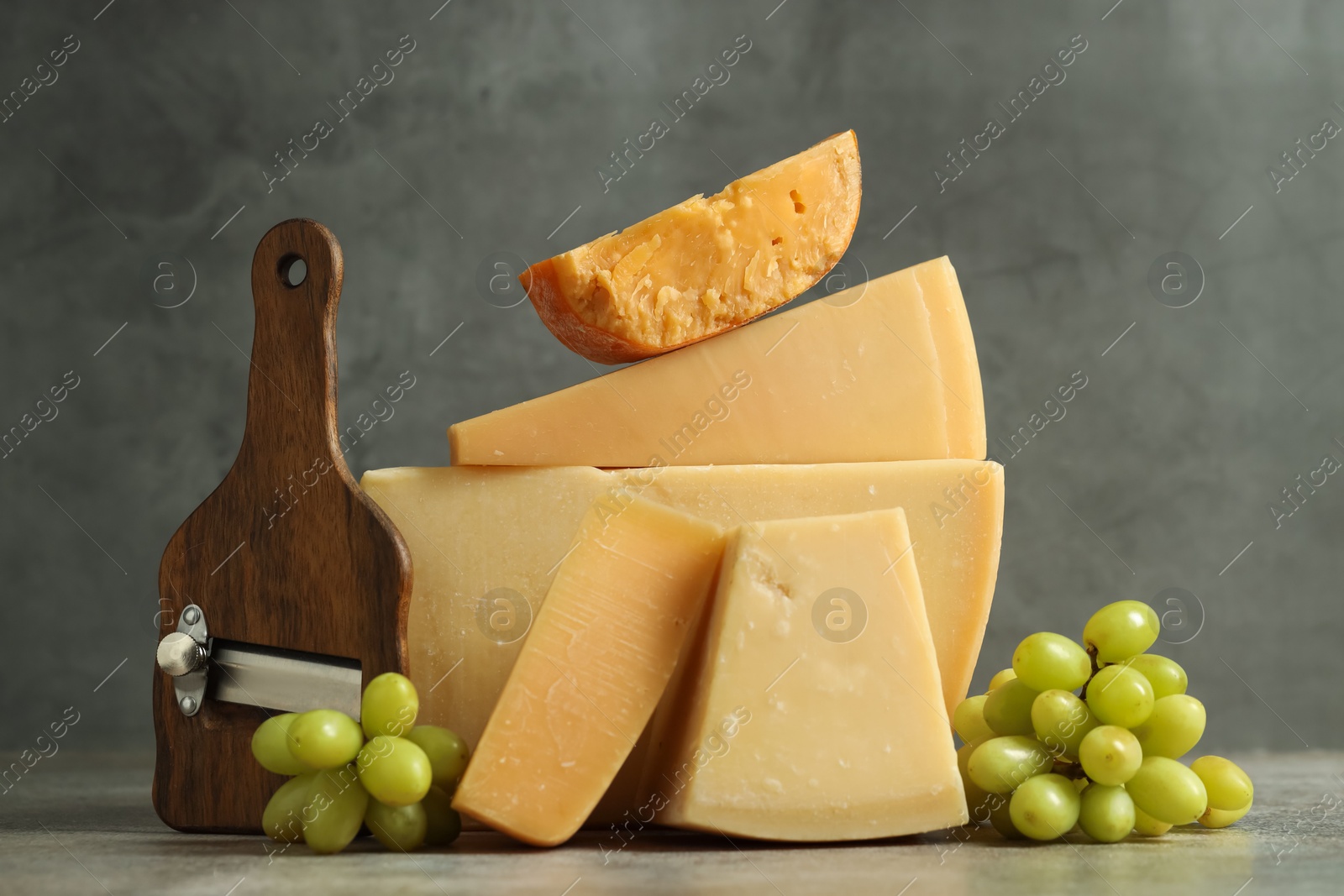 Photo of Different types of cheese, slicer and grapes on grey table