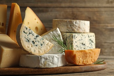 Photo of Different types of cheese and rosemary on wooden table, closeup