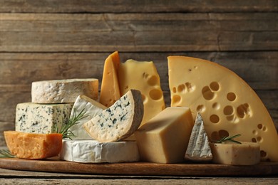 Photo of Different types of cheese and rosemary on wooden table