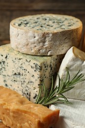 Photo of Different types of cheese and rosemary on blurred background, closeup