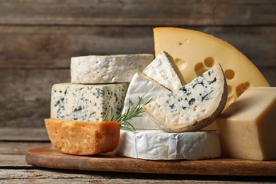 Photo of Different types of cheese and rosemary on wooden table, closeup