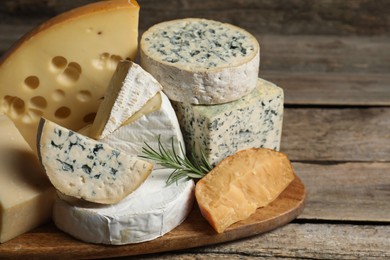 Photo of Different types of cheese and rosemary on wooden table, closeup. Space for text