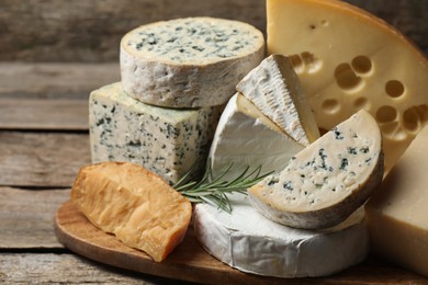 Photo of Different types of cheese and rosemary on wooden table, closeup