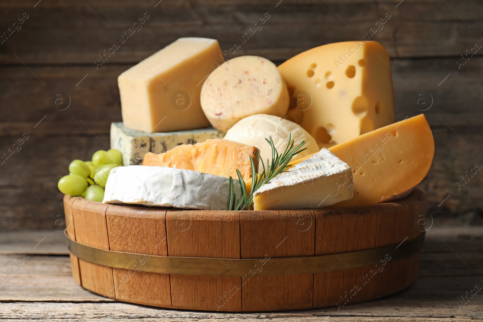 Photo of Different types of cheese, rosemary and grapes on wooden table, closeup