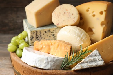 Photo of Different types of cheese, rosemary and grapes in wooden tray on table, closeup