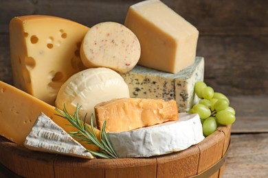 Photo of Different types of cheese, rosemary and grapes in wooden tray on table, closeup