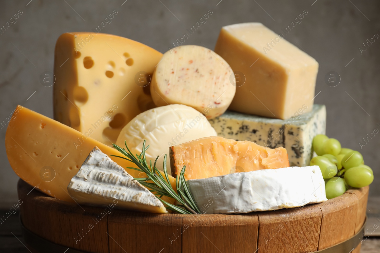 Photo of Different types of cheese, rosemary and grapes in wooden tray on table, closeup