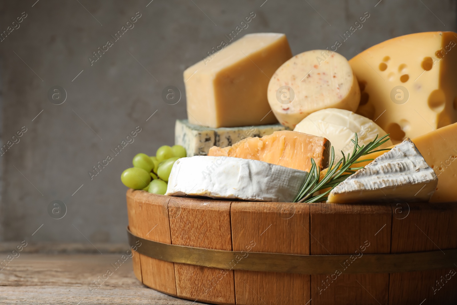 Photo of Different types of cheese, rosemary and grapes on wooden table, closeup. Space for text