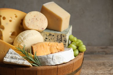 Photo of Different types of cheese, rosemary and grapes on wooden table, closeup. Space for text