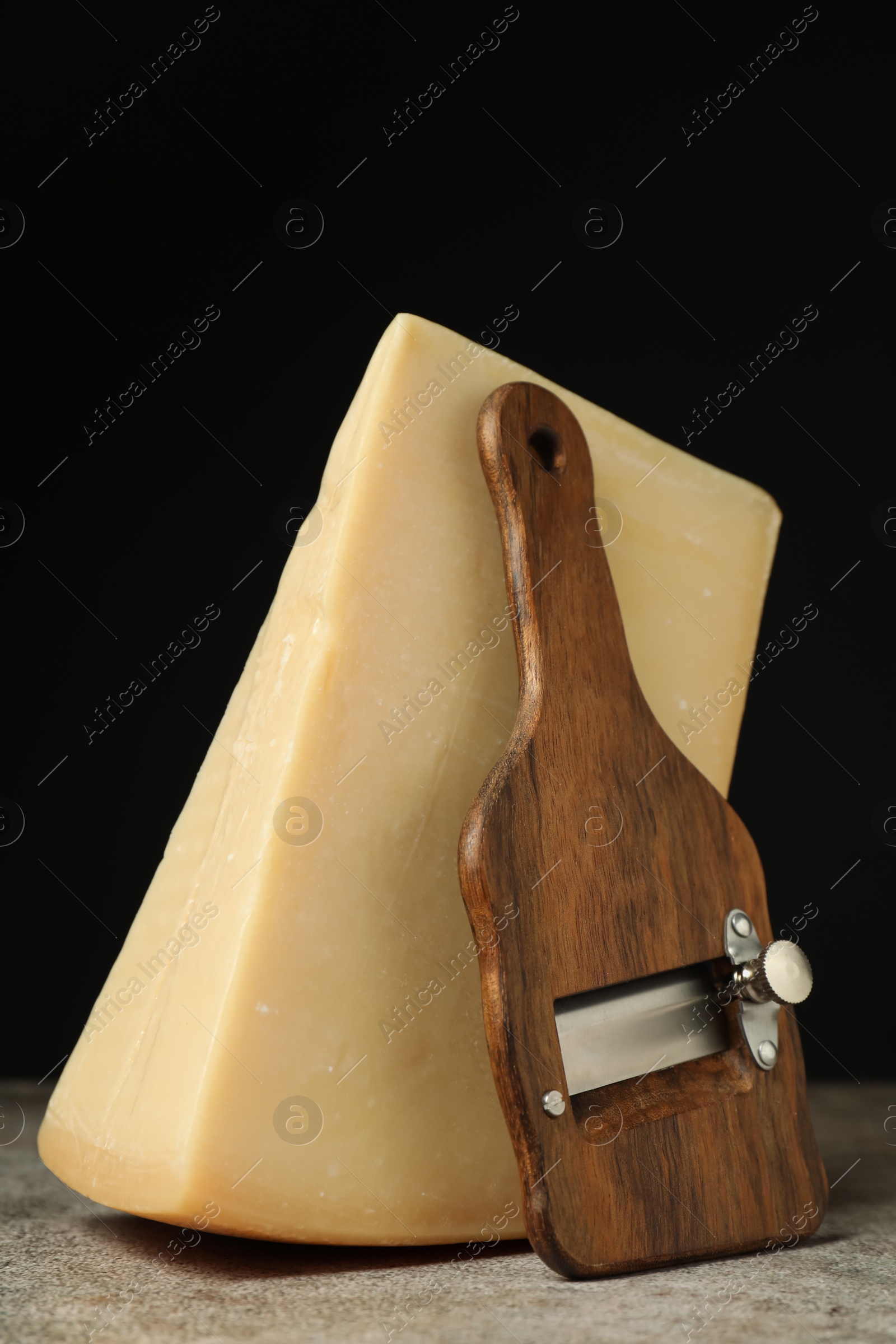 Photo of Piece of tasty cheese and slicer on grey table, closeup