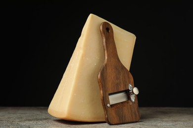 Photo of Piece of tasty cheese and slicer on grey table, closeup