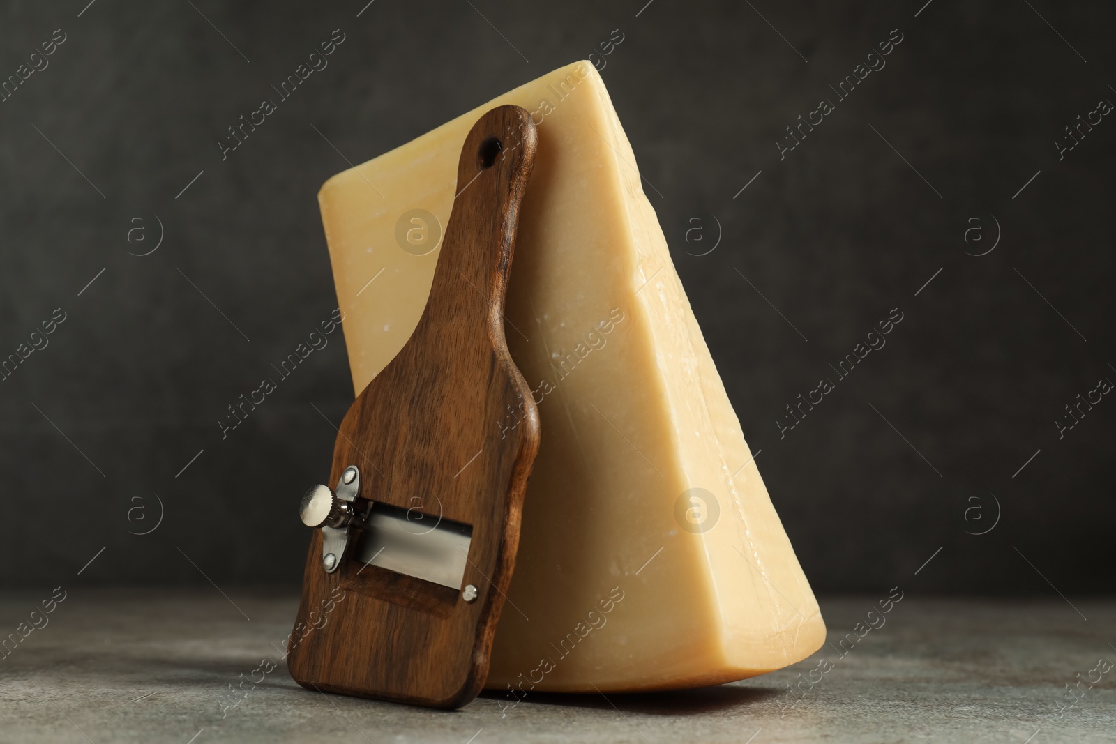 Photo of Piece of tasty cheese and slicer on grey table, closeup