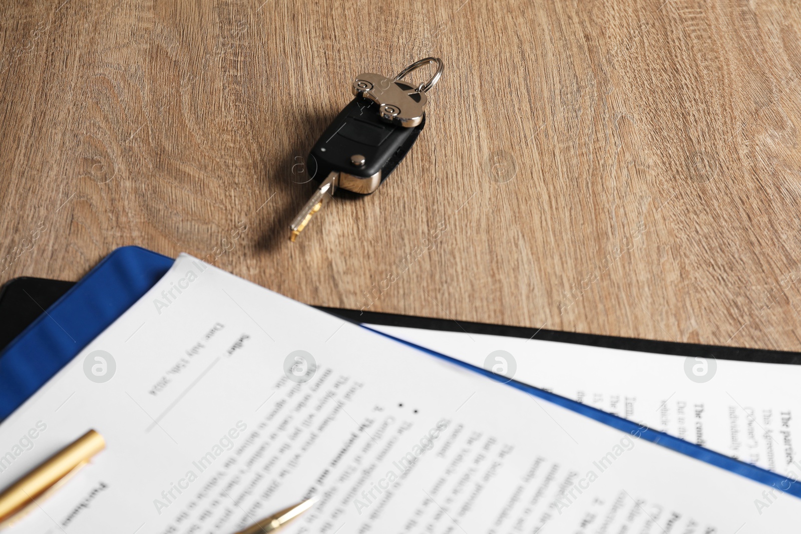 Photo of Car key and purchase agreement on wooden table, closeup. Buying auto