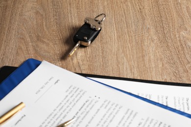 Photo of Car key and purchase agreement on wooden table, closeup. Buying auto