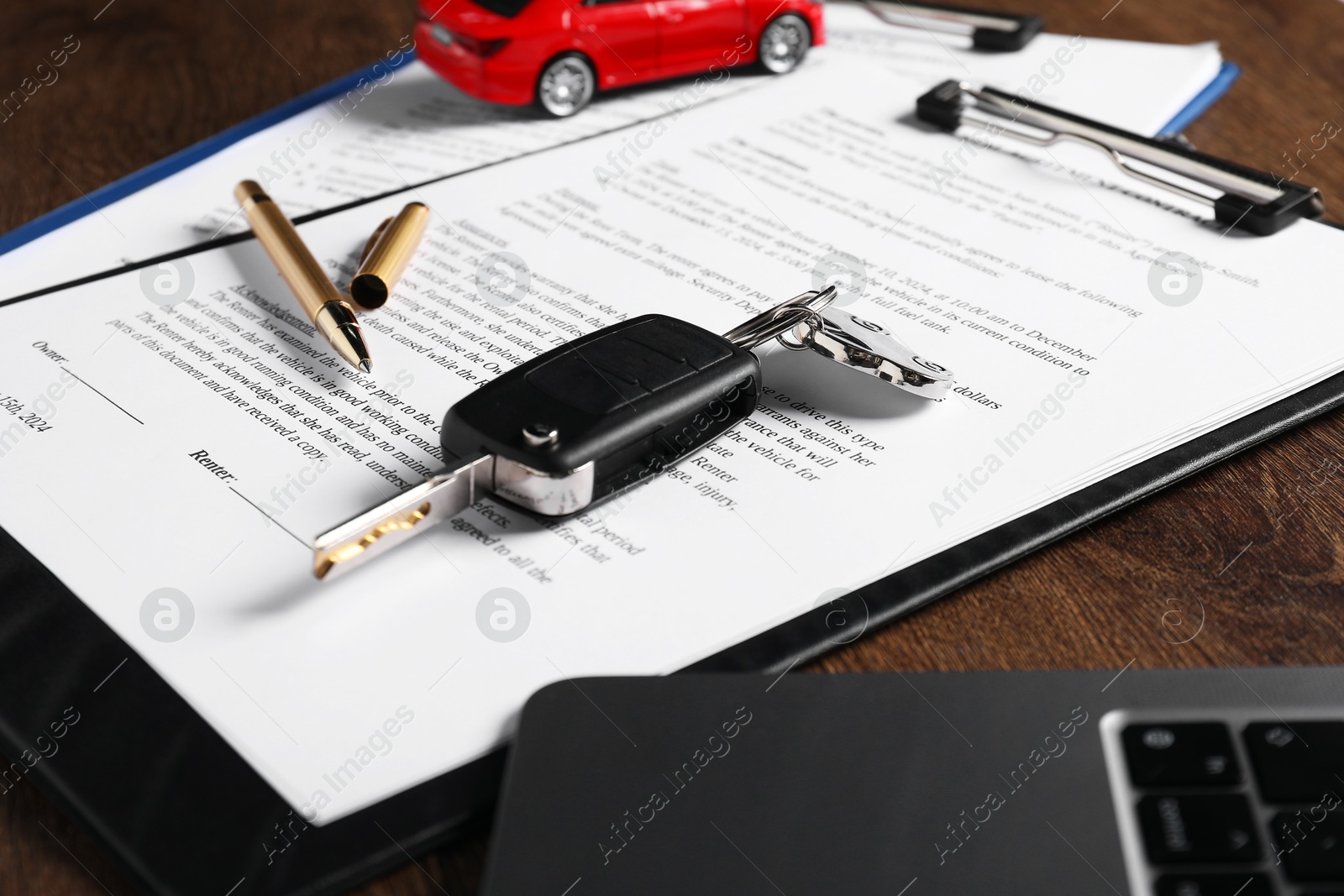 Photo of Car key, model, laptop and purchase agreement on wooden table, closeup. Buying auto