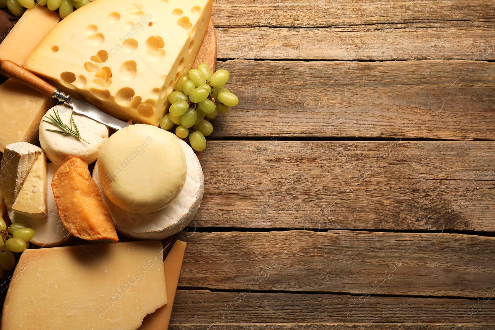 Photo of Different types of cheese, rosemary and grapes on wooden table, flat lay. Space for text