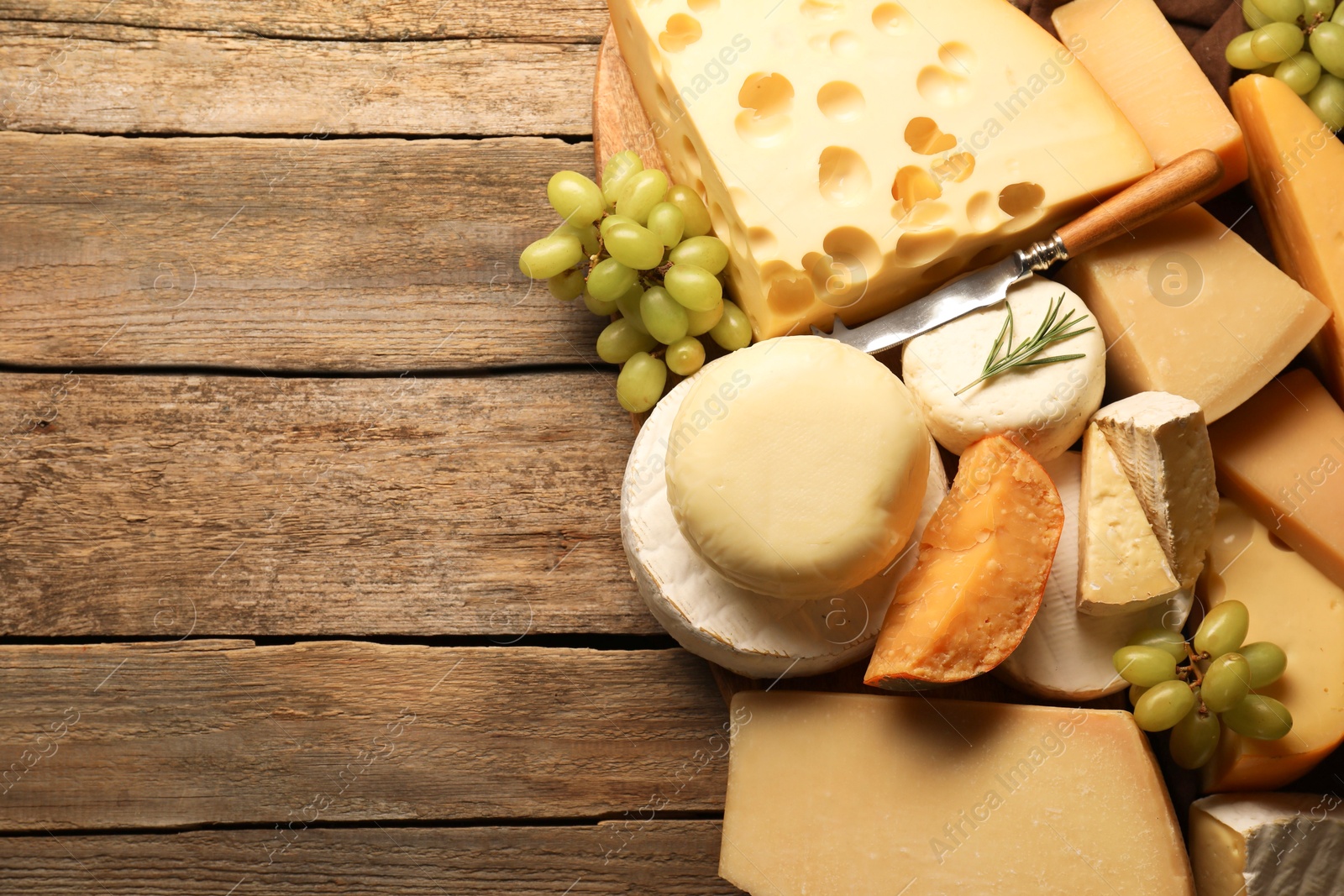 Photo of Different types of cheese, rosemary and grapes on wooden table, flat lay. Space for text