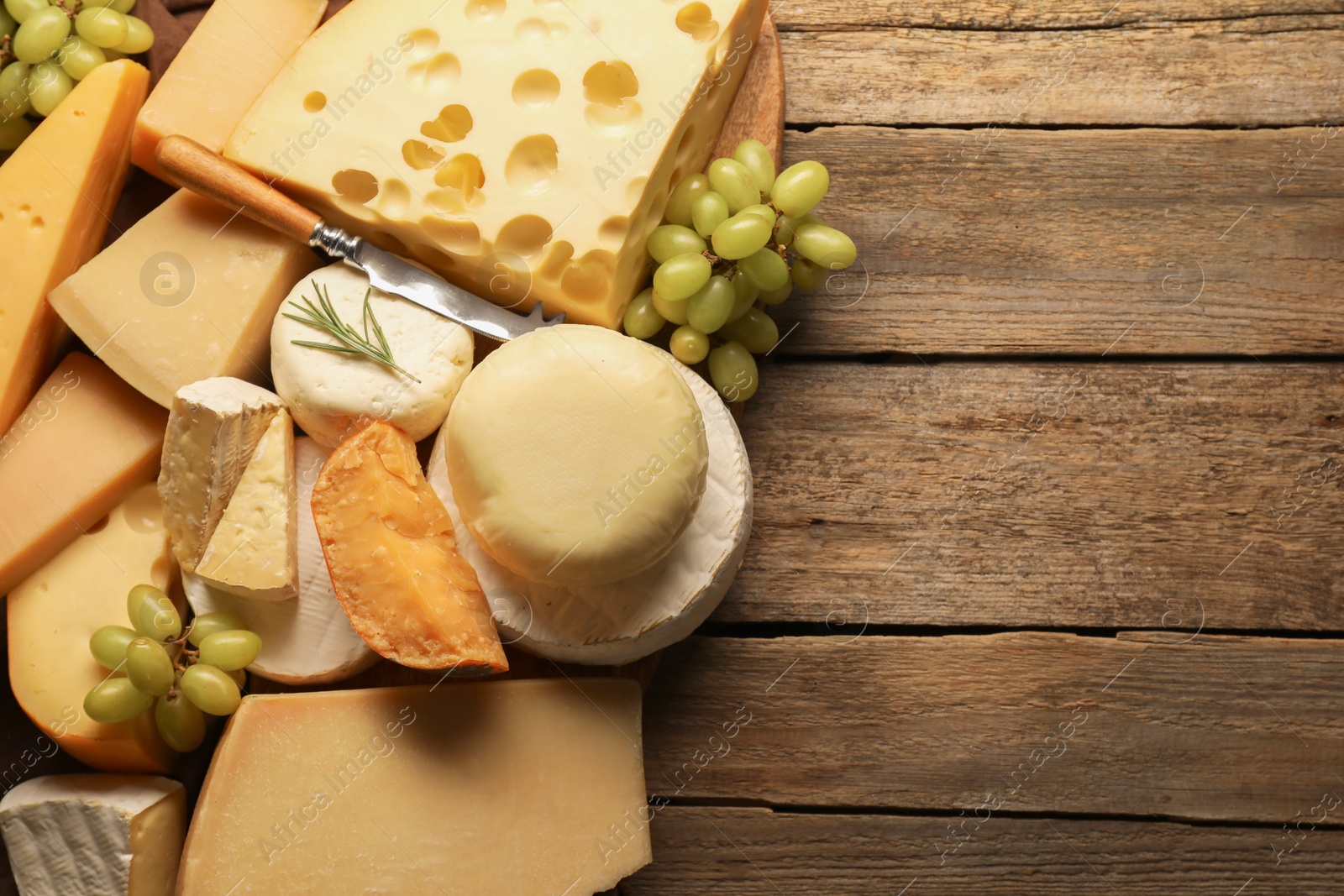 Photo of Different types of cheese, rosemary and grapes on wooden table, flat lay. Space for text