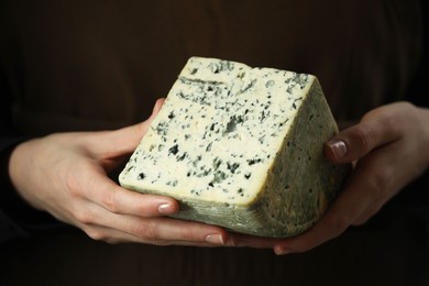 Photo of Woman with piece of delicious cheese on dark background, closeup