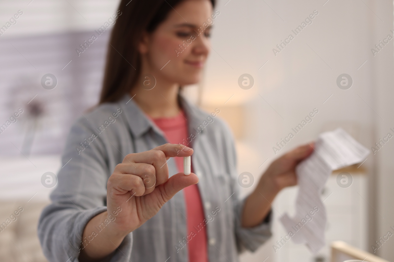 Photo of Woman with pill reading instruction at home, selective focus