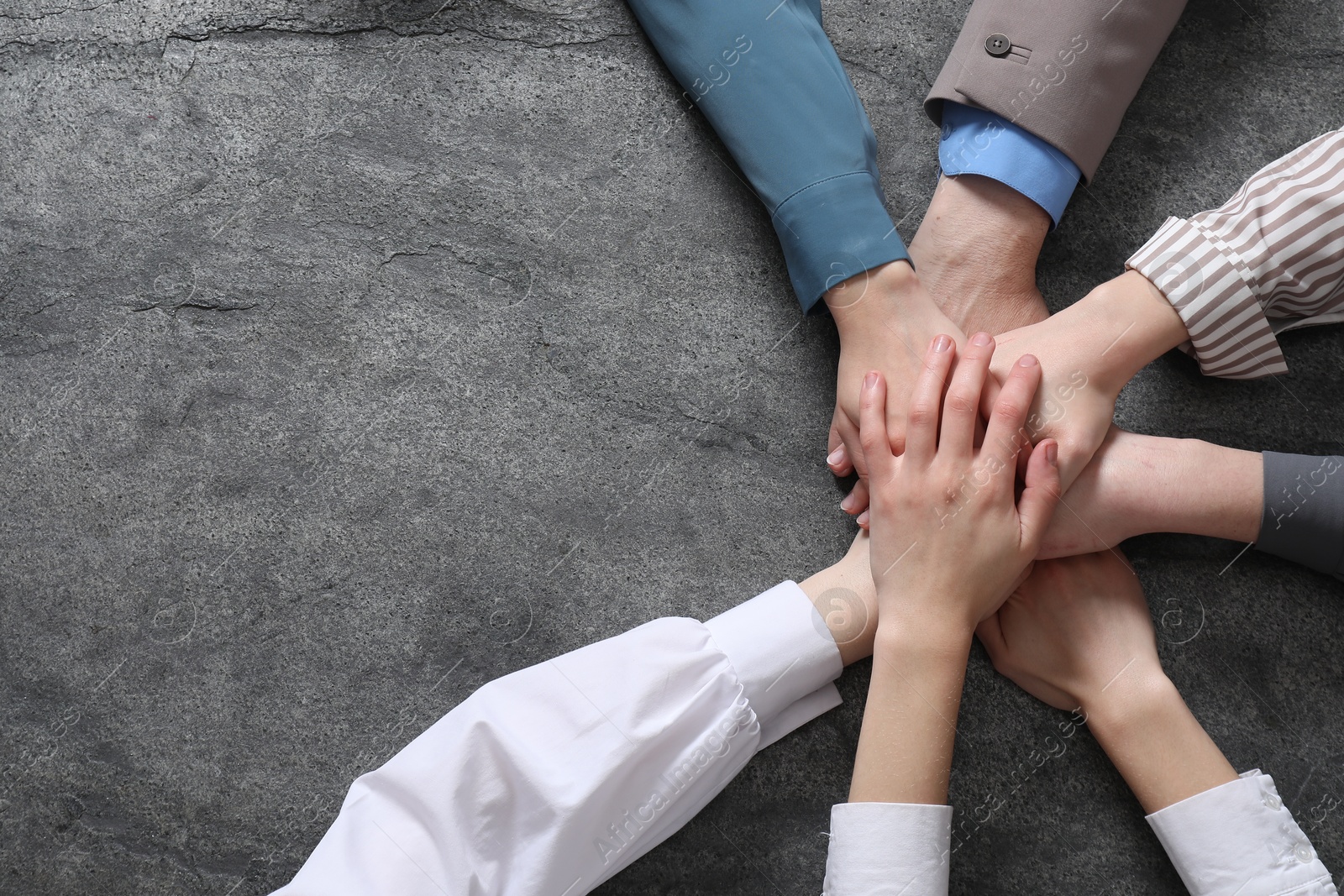 Photo of Business concept. Group of people stacking hands at grey textured table, top view. Space for text