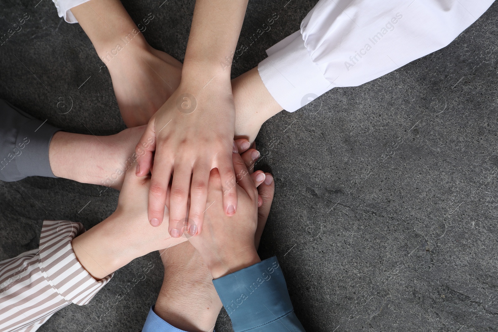 Photo of Business concept. Group of people stacking hands at grey textured table, top view. Space for text