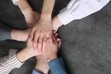 Photo of Business concept. Group of people stacking hands at grey textured table, top view. Space for text