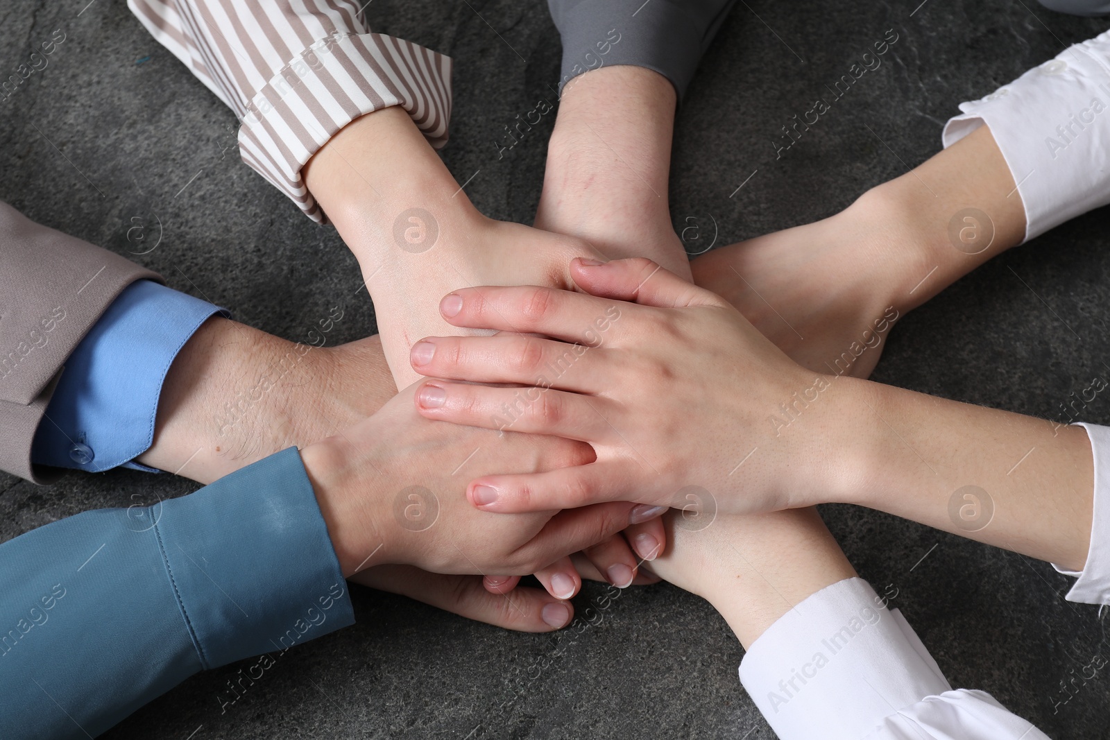 Photo of Business concept. Group of people stacking hands at grey textured table, above view