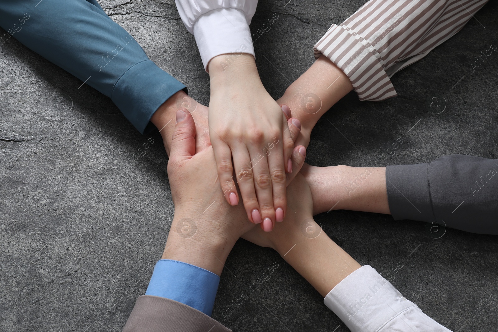 Photo of Business concept. Group of people stacking hands at grey textured table, top view