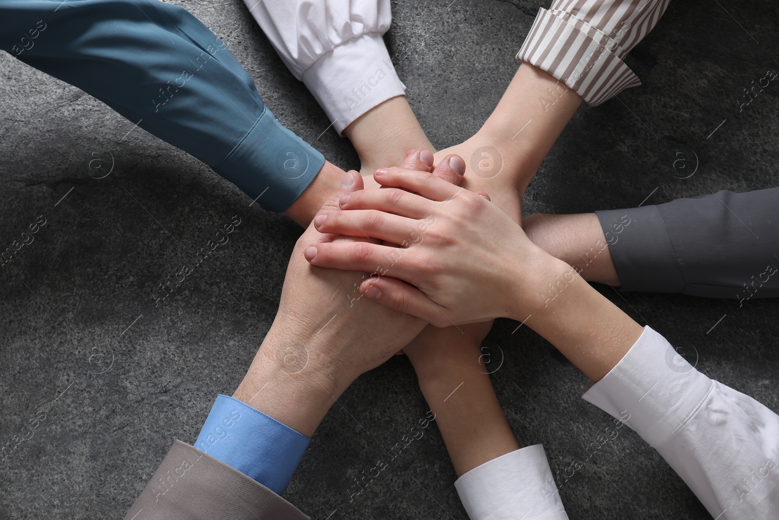 Photo of Business concept. Group of people stacking hands at grey textured table, top view